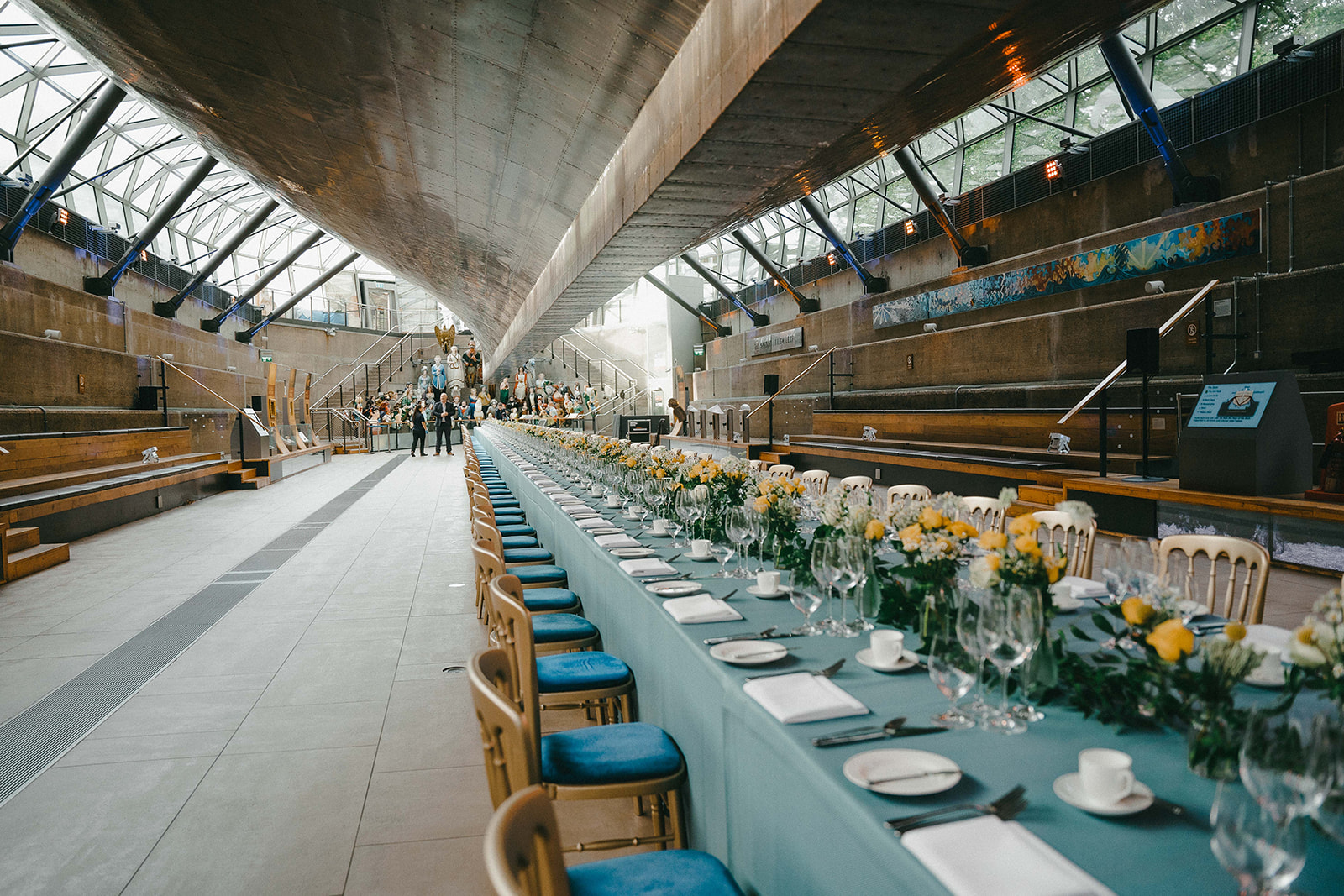 View of the great hall beneath the Cutty Sark with a long dining table in teal and yellow.