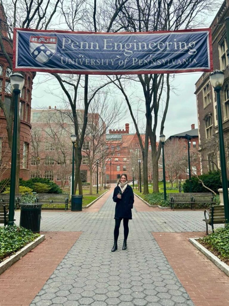 Alice stands on Locust Walk at Penn under a banner for Penn Engineering