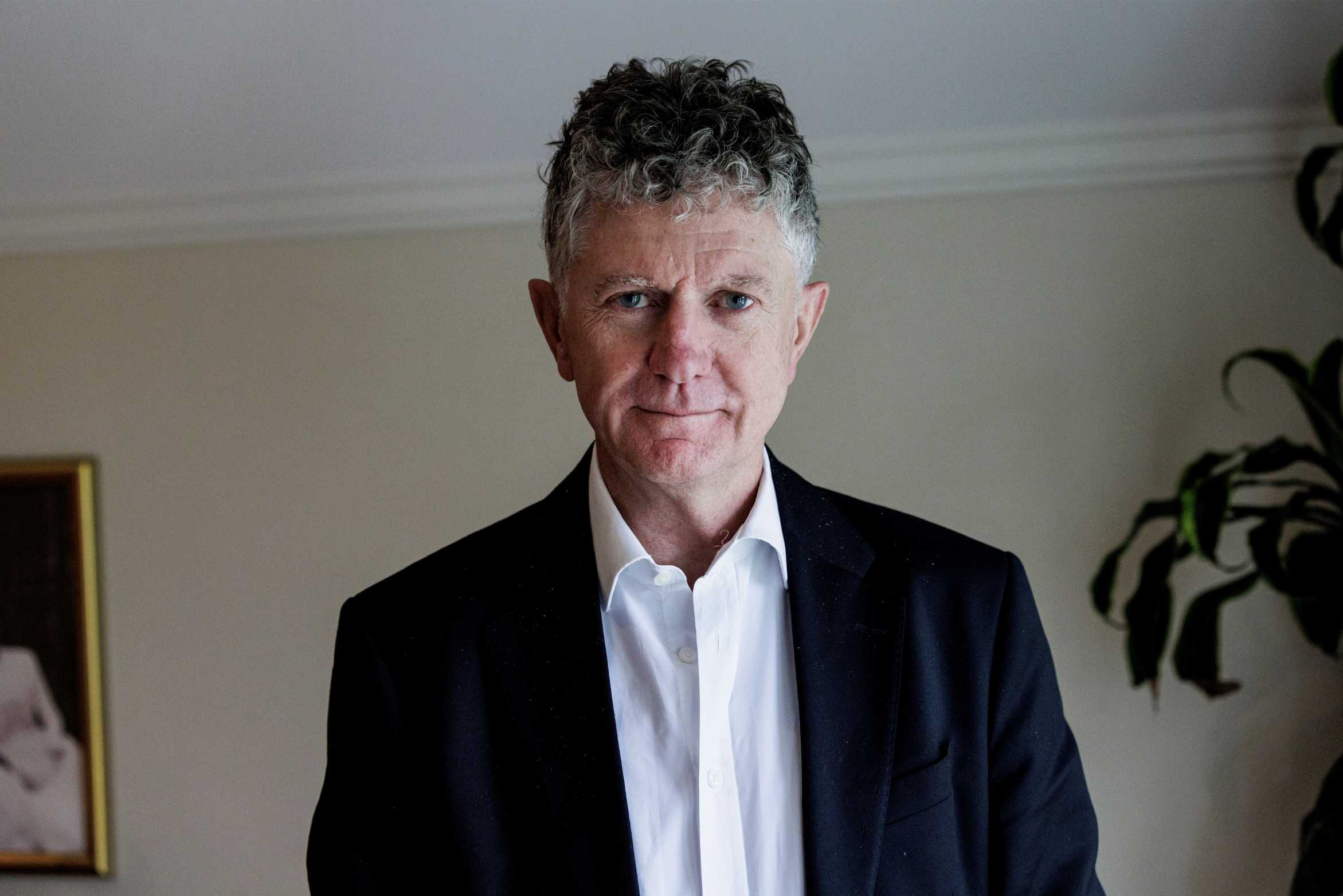 Jonathan Powell stands in office in white button up and suit jacket